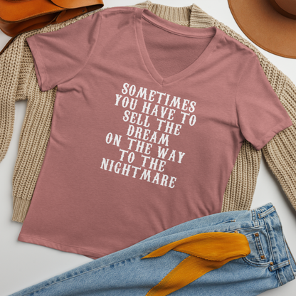 "Sometimes you have to sell the dream on the way to the nightmare" printed on a heather mauve women's relaxed v-neck t-shirt laying on a flat surface amongst other clothes