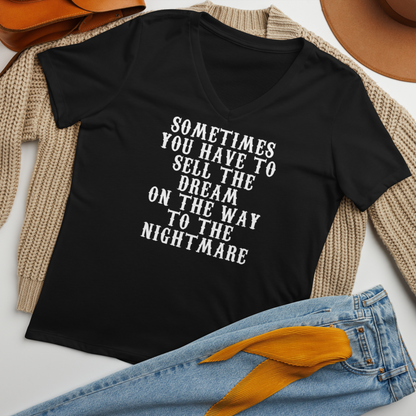 "Sometimes you have to sell the dream on the way to the nightmare" printed on a solid black blend women's relaxed v-neck t-shirt laying on a flat surface amongst other clothes