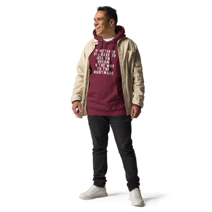 "Sometimes you have to sell the dream on the way to the nightmare" printed on a maroon unisex hoodie worn by a male with a jacket on top