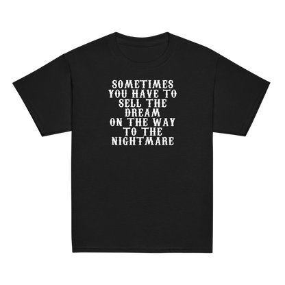 "Sometimes you have to sell the dream on the way to the nightmare" printed on a black youth classic tee laying on a flat surface