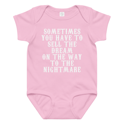 "Sometimes you have to sell the dream on the way to the nightmare" printed on a pink baby jersey bodysuit laying on a flat surface amongst other clothes