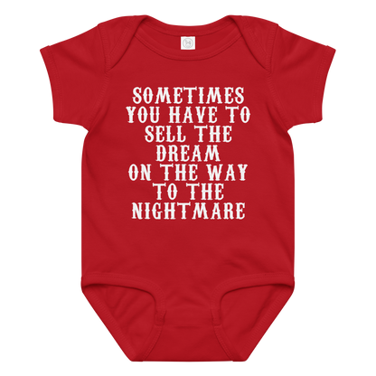 "Sometimes you have to sell the dream on the way to the nightmare" printed on a red baby jersey bodysuit laying on a flat surface amongst other clothes