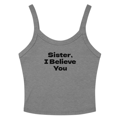 "Sister, I Believe You!" printed on a athletic heather women's micro-rib tanktop laying on a flat surface amongst sunglasses and shorts