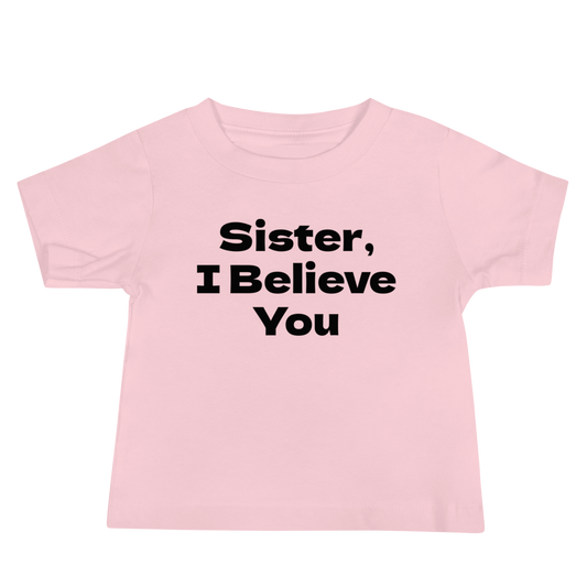 "Sister, I Believe You!" printed on a pink baby jersey short sleeve tee laying on a flat surface