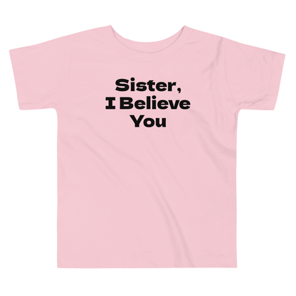 "Sister, I Believe You!" printed on a pink toddler short sleeve tee laying on a flat surface