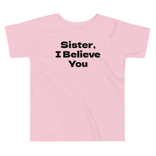 "Sister, I Believe You!" printed on a pink toddler short sleeve tee laying on a flat surface