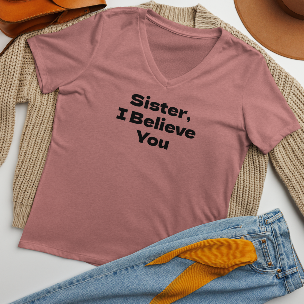 "Sister, I Believe You!" printed on a heather mauve women's relaxed v-neck t-shirt laying on a flat surface amongst other clothes