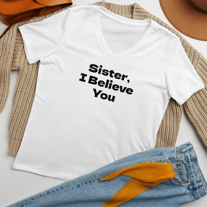 "Sister, I Believe You!" printed on a solid white blend women's relaxed v-neck t-shirt laying on a flat surface amongst other clothes