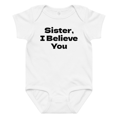 "Sister, I Believe You!" printed on a white baby jersey bodysuit laying on a flat surface amongst other clothes