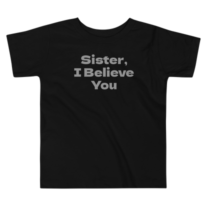 "Sister, I Believe You!" printed on a black toddler short sleeve tee laying on a flat surface