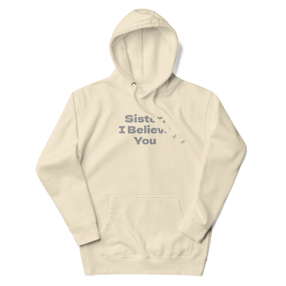 "Sister, I Believe You!" printed on a bone unisex hoodie laying on a flat surface with the hood up