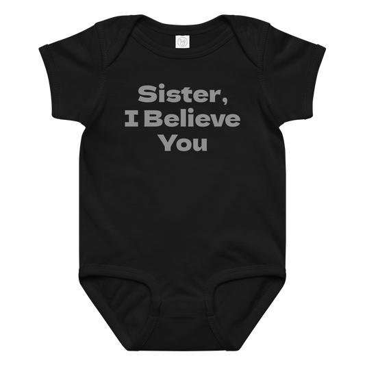 "Sister, I Believe You!" printed on a black baby jersey bodysuit laying on a flat surface amongst other clothes