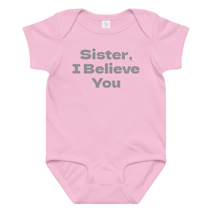 "Sister, I Believe You!" printed on a pink baby jersey bodysuit laying on a flat surface amongst other clothes