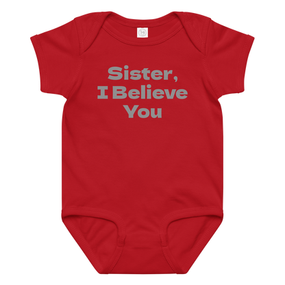 "Sister, I Believe You!" printed on a red baby jersey bodysuit laying on a flat surface amongst other clothes