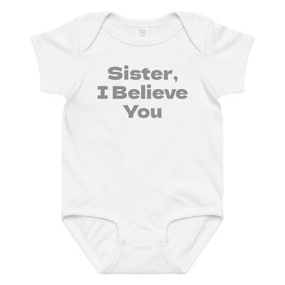 "Sister, I Believe You!" printed on a white baby jersey bodysuit laying on a flat surface amongst other clothes