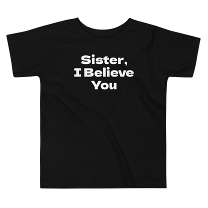 "Sister, I Believe You!" printed on a black toddler short sleeve tee laying on a flat surface