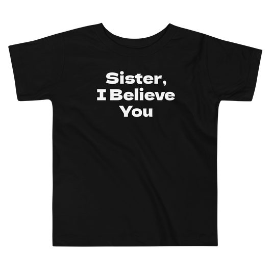 "Sister, I Believe You!" printed on a black toddler short sleeve tee laying on a flat surface
