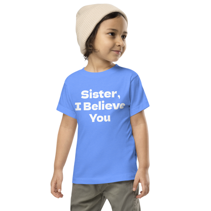 "Sister, I Believe You!" printed on a heather columbia blue toddler short sleeve tee worn by a male wearing a cap