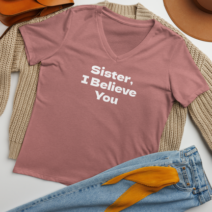 "Sister, I Believe You!" printed on a heather mauve women's relaxed v-neck t-shirt laying on a flat surface amongst other clothes