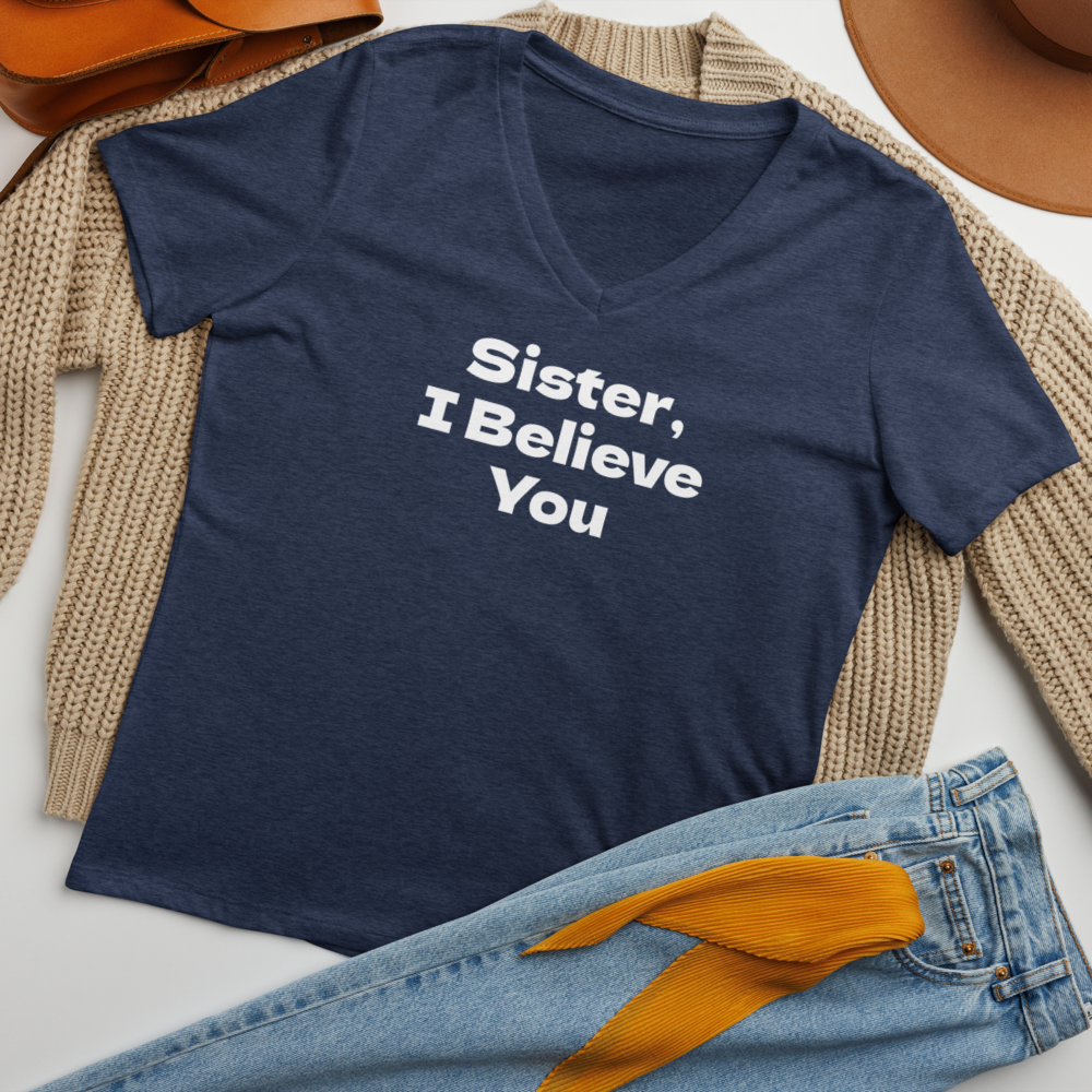 "Sister, I Believe You!" printed on a heather navy women's relaxed v-neck t-shirt laying on a flat surface amongst other clothes