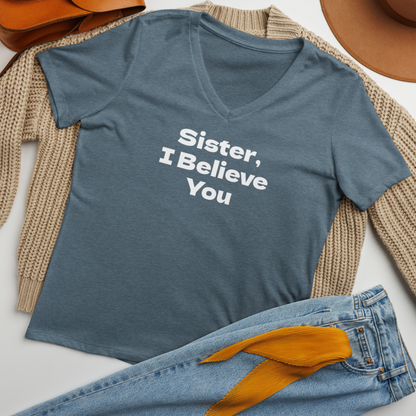 "Sister, I Believe You!" printed on a heather slate women's relaxed v-neck t-shirt laying on a flat surface amongst other clothes