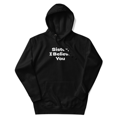 "Sister, I Believe You!" printed on a black unisex hoodie laying on a flat surface with the hood up