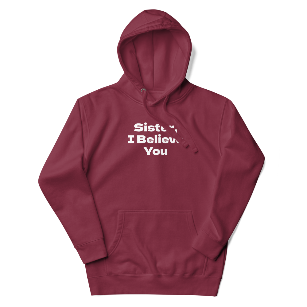 "Sister, I Believe You!" printed on a maroon unisex hoodie laying on a flat surface with the hood up