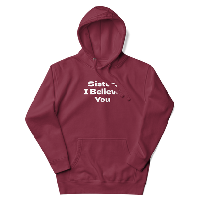 "Sister, I Believe You!" printed on a maroon unisex hoodie laying on a flat surface with the hood up