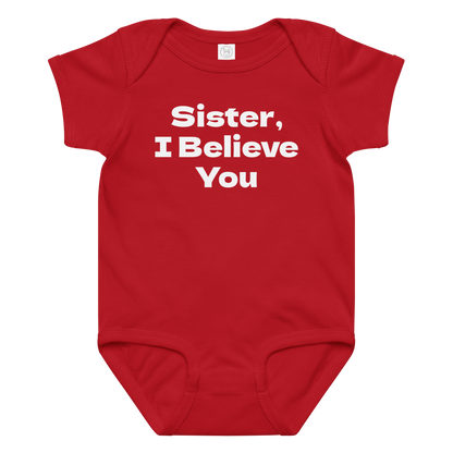 "Sister, I Believe You!" printed on a red baby jersey bodysuit laying on a flat surface amongst other clothes