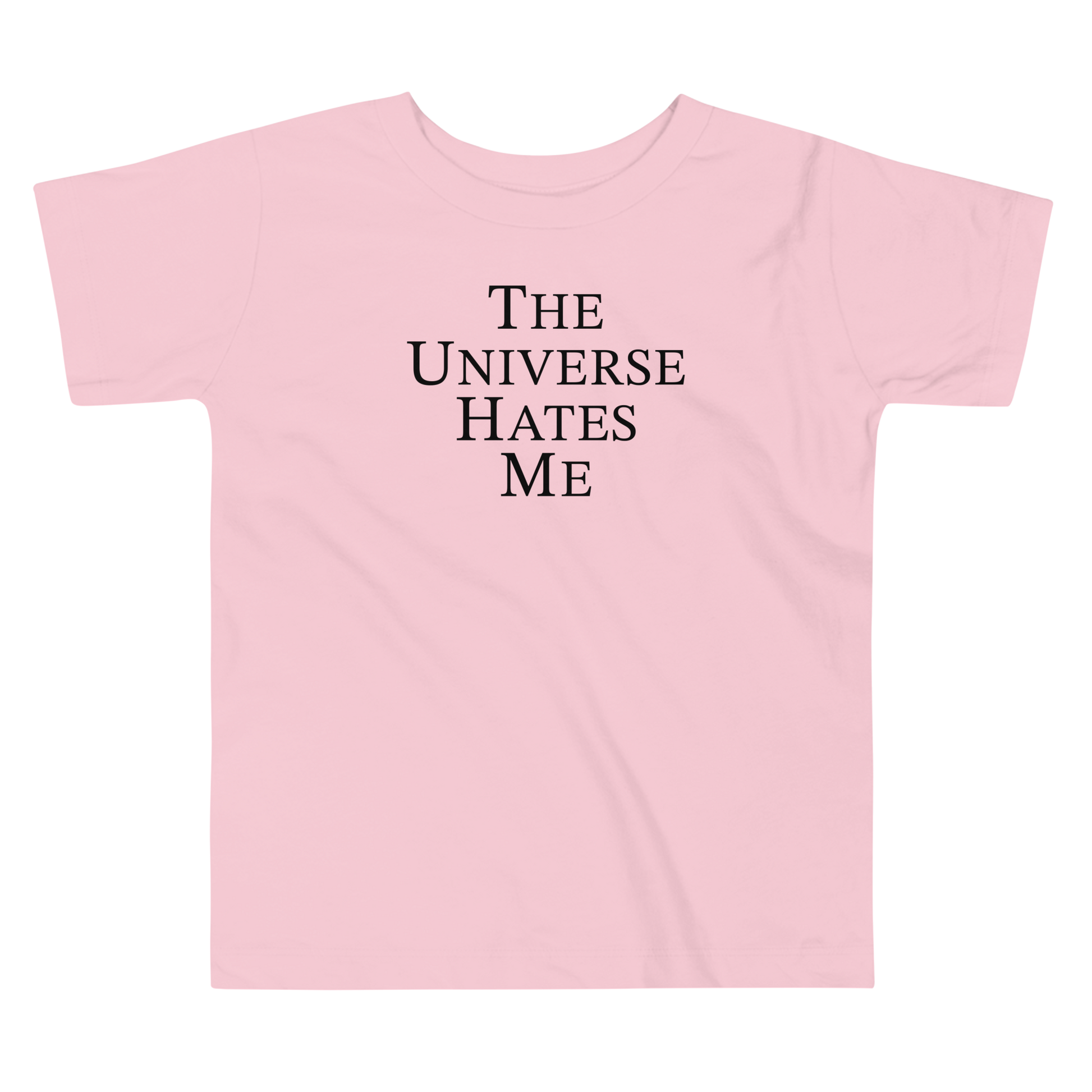 "The Universe Hates Me" printed on a pink toddler short sleeve tee laying on a flat surface