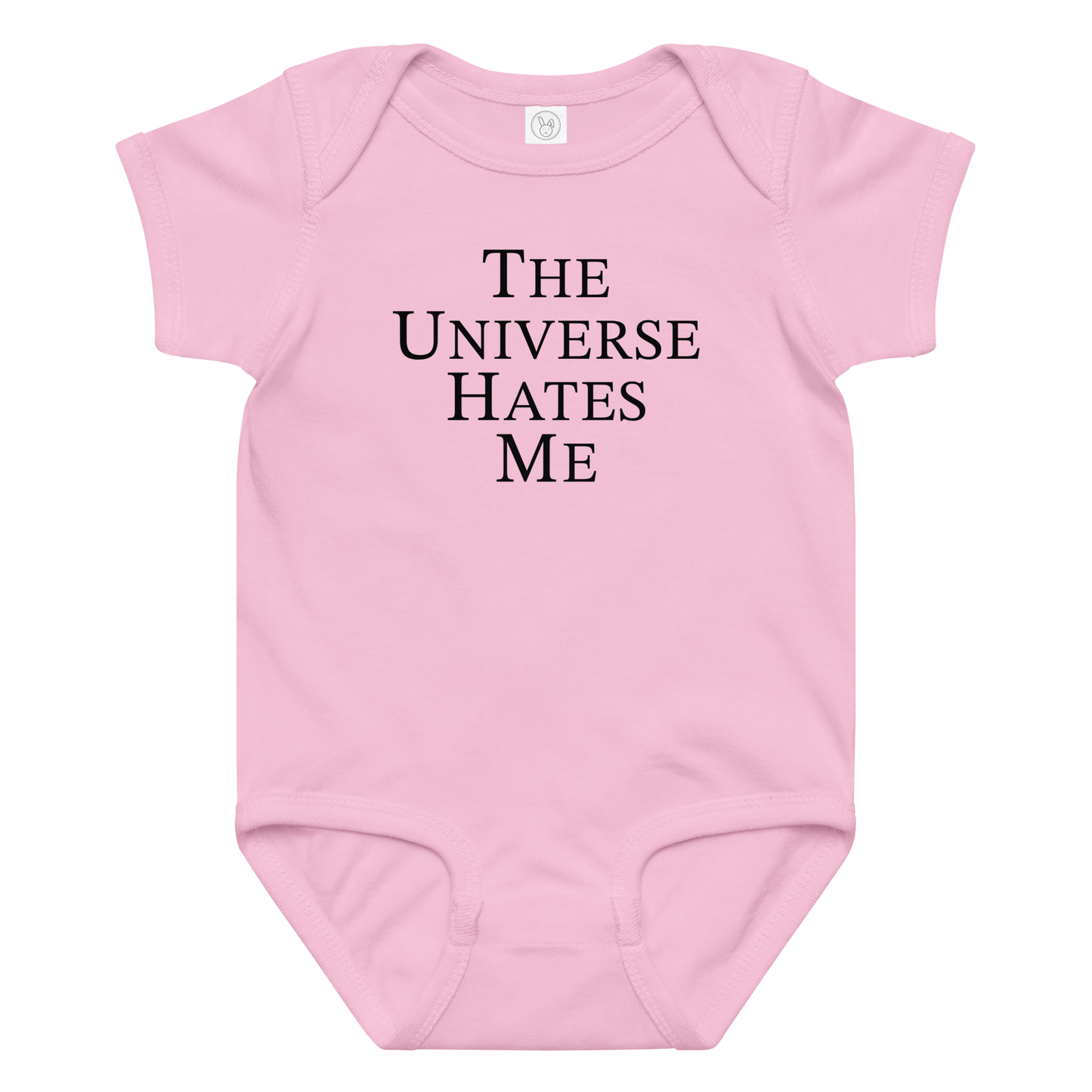"The Universe Hates Me" printed on a pink baby jersey bodysuit laying on a flat surface amongst other clothes