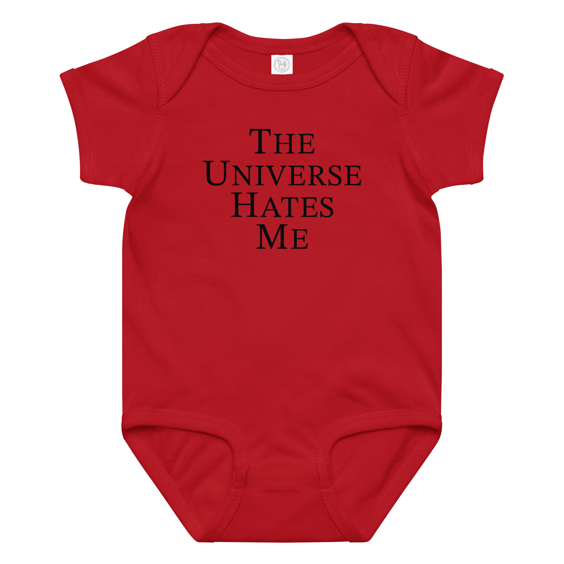 "The Universe Hates Me" printed on a red baby jersey bodysuit laying on a flat surface amongst other clothes