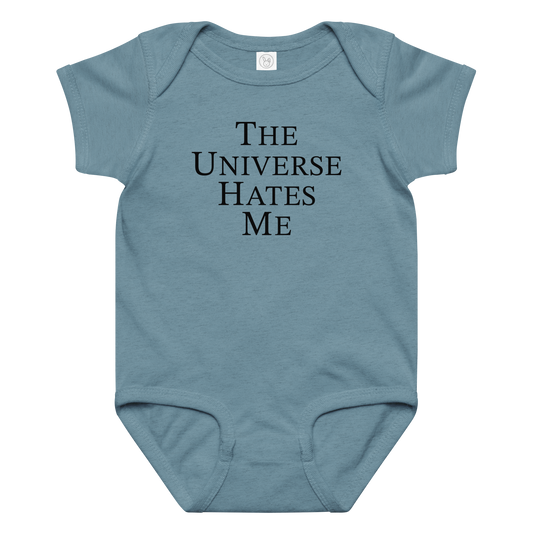 "The Universe Hates Me" printed on a vintage indigo baby jersey bodysuit laying on a flat surface amongst other clothes