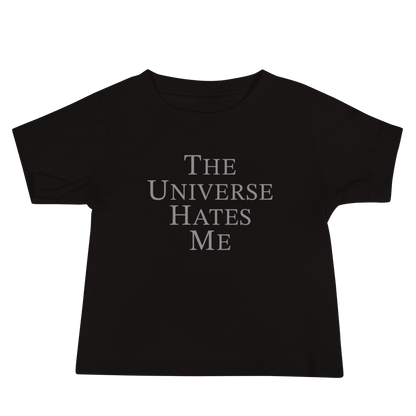 "The Universe Hates Me" printed on a black baby jersey short sleeve tee laying on a flat surface