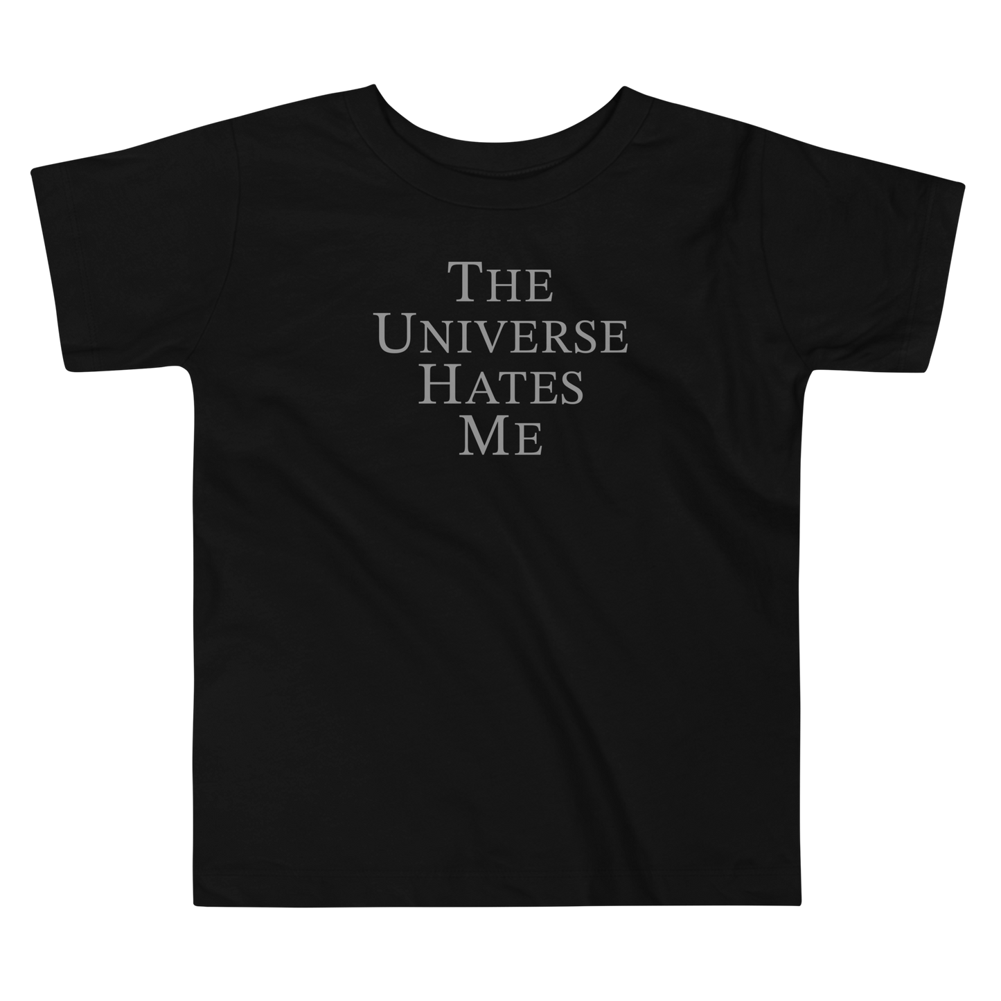 "The Universe Hates Me" printed on a black toddler short sleeve tee laying on a flat surface