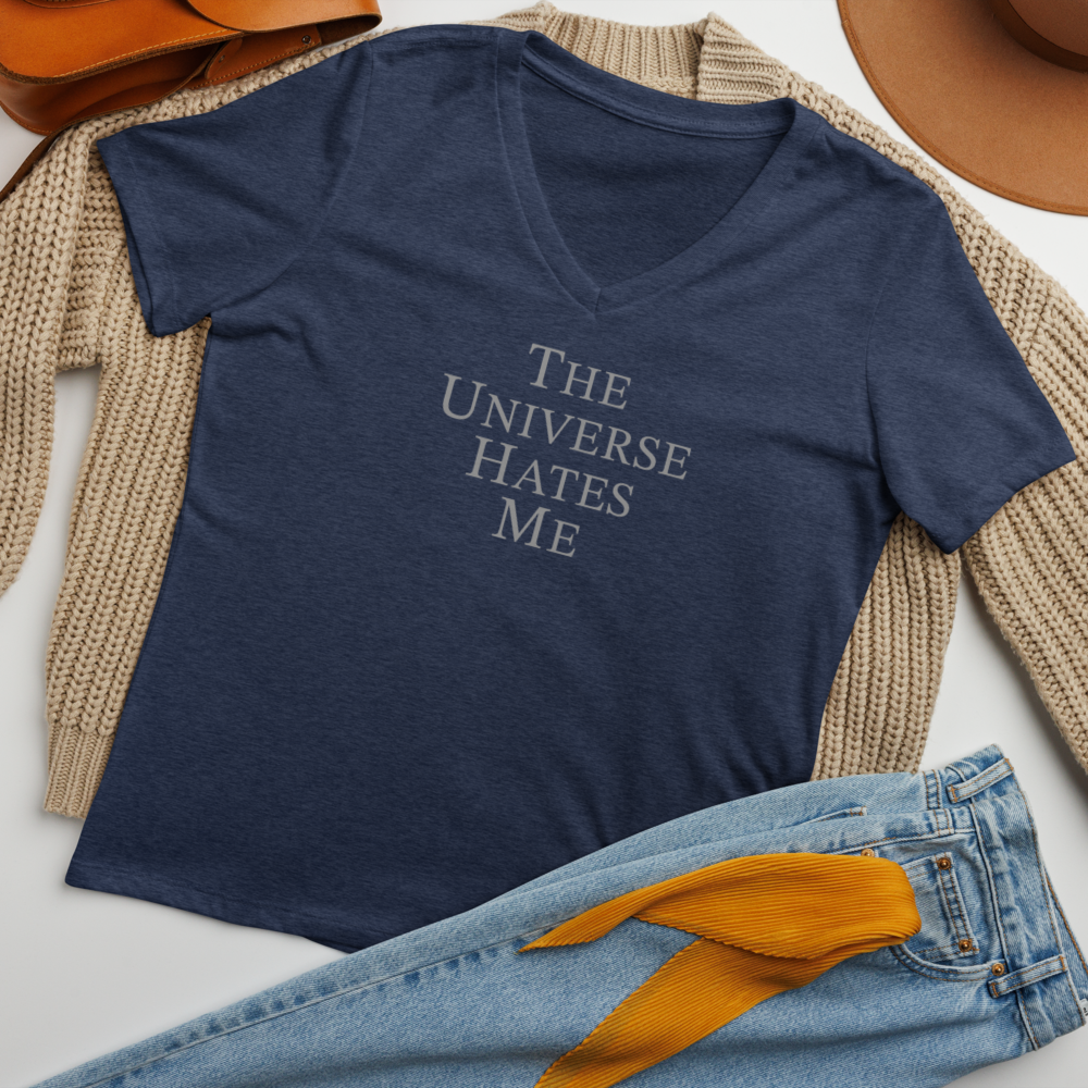 "The Universe Hates Me" printed on a heather navy women's relaxed v-neck t-shirt laying on a flat surface amongst other clothes
