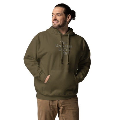 "The Universe Hates Me" printed on a military green unisex hoodie worn by a male