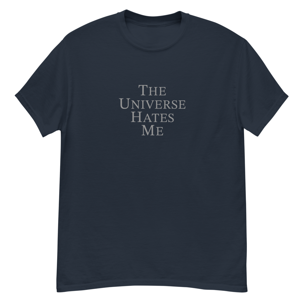 "The Universe Hates Me" printed on a navy unisex classic tee laying on a flat surface