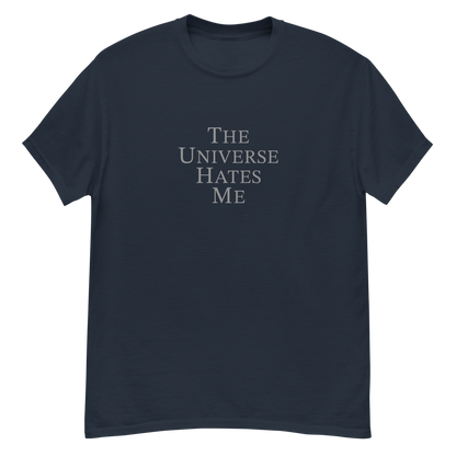 "The Universe Hates Me" printed on a navy unisex classic tee laying on a flat surface