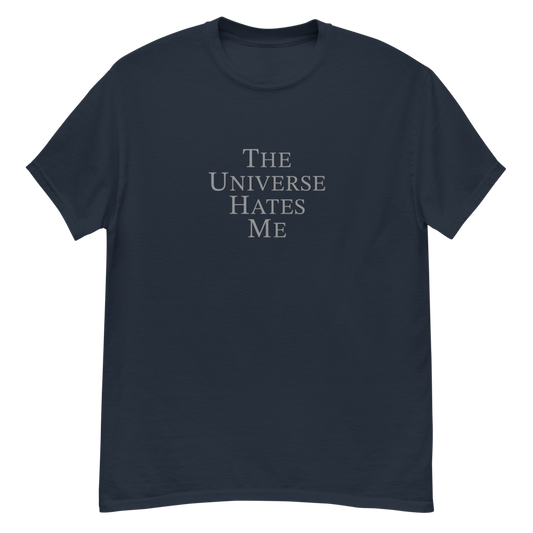 "The Universe Hates Me" printed on a navy unisex classic tee laying on a flat surface