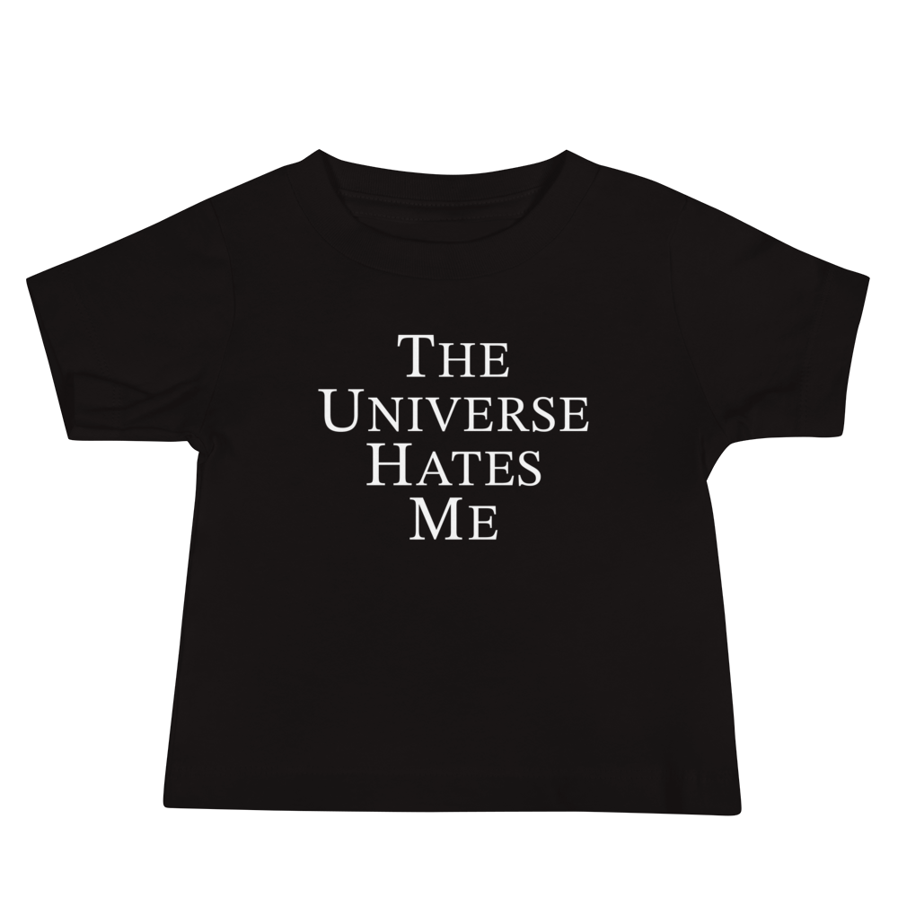"The Universe Hates Me" printed on a black baby jersey short sleeve tee laying on a flat surface