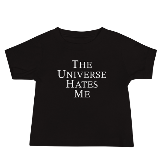 "The Universe Hates Me" printed on a black baby jersey short sleeve tee laying on a flat surface
