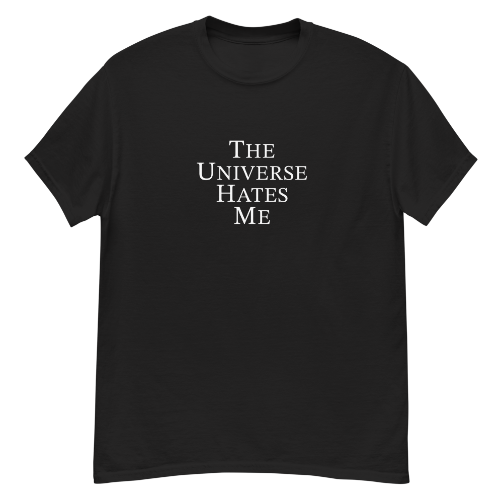 "The Universe Hates Me" printed on a black unisex classic tee laying on a flat surface