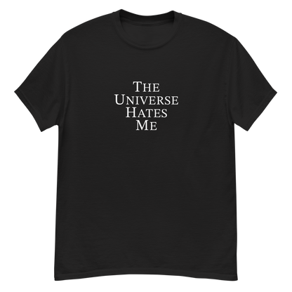 "The Universe Hates Me" printed on a black unisex classic tee laying on a flat surface