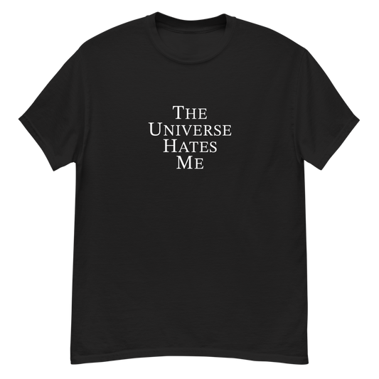 "The Universe Hates Me" printed on a black unisex classic tee laying on a flat surface