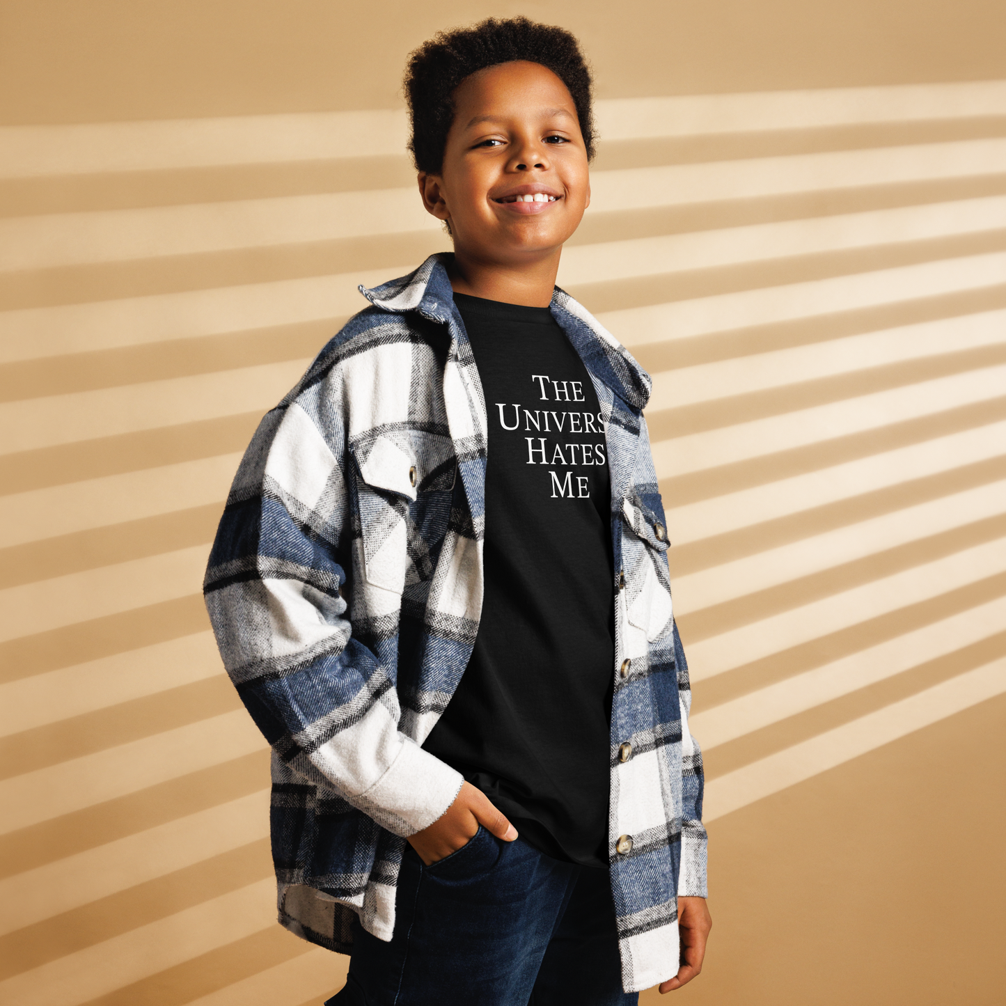 "The Universe Hates Me" printed on a black youth classic tee worn by a male also wearing a jacket