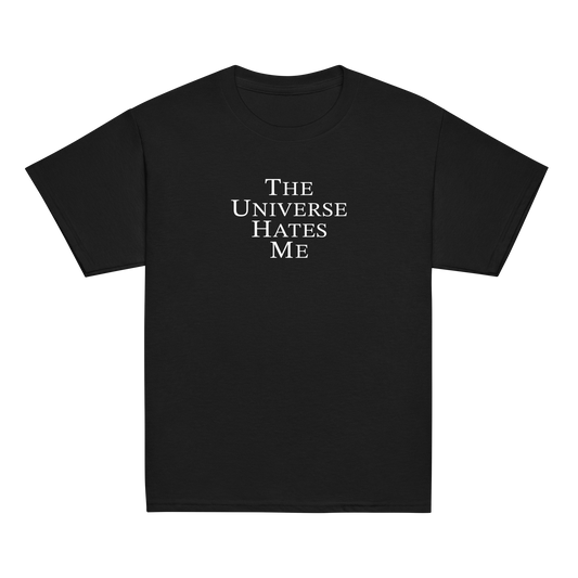 "The Universe Hates Me" printed on a black youth classic tee laying on a flat surface