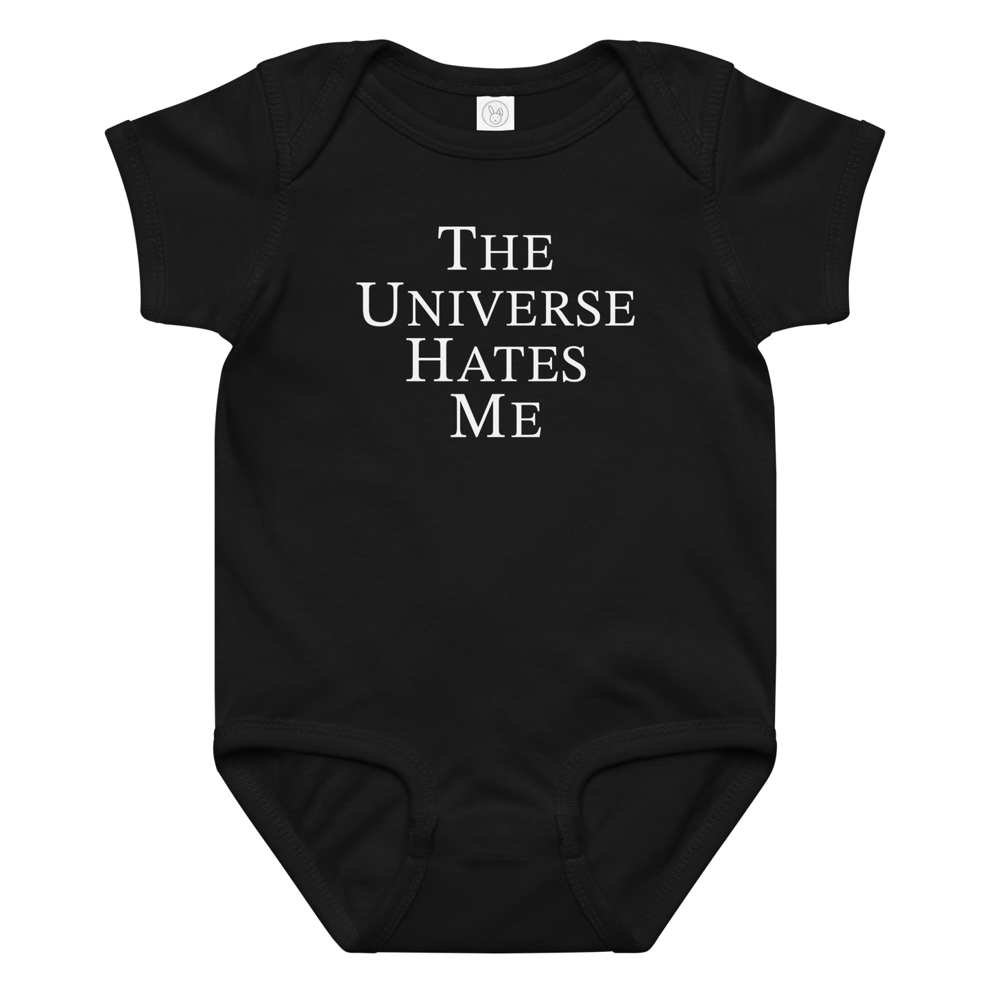 "The Universe Hates Me" printed on a black baby jersey bodysuit laying on a flat surface amongst other clothes