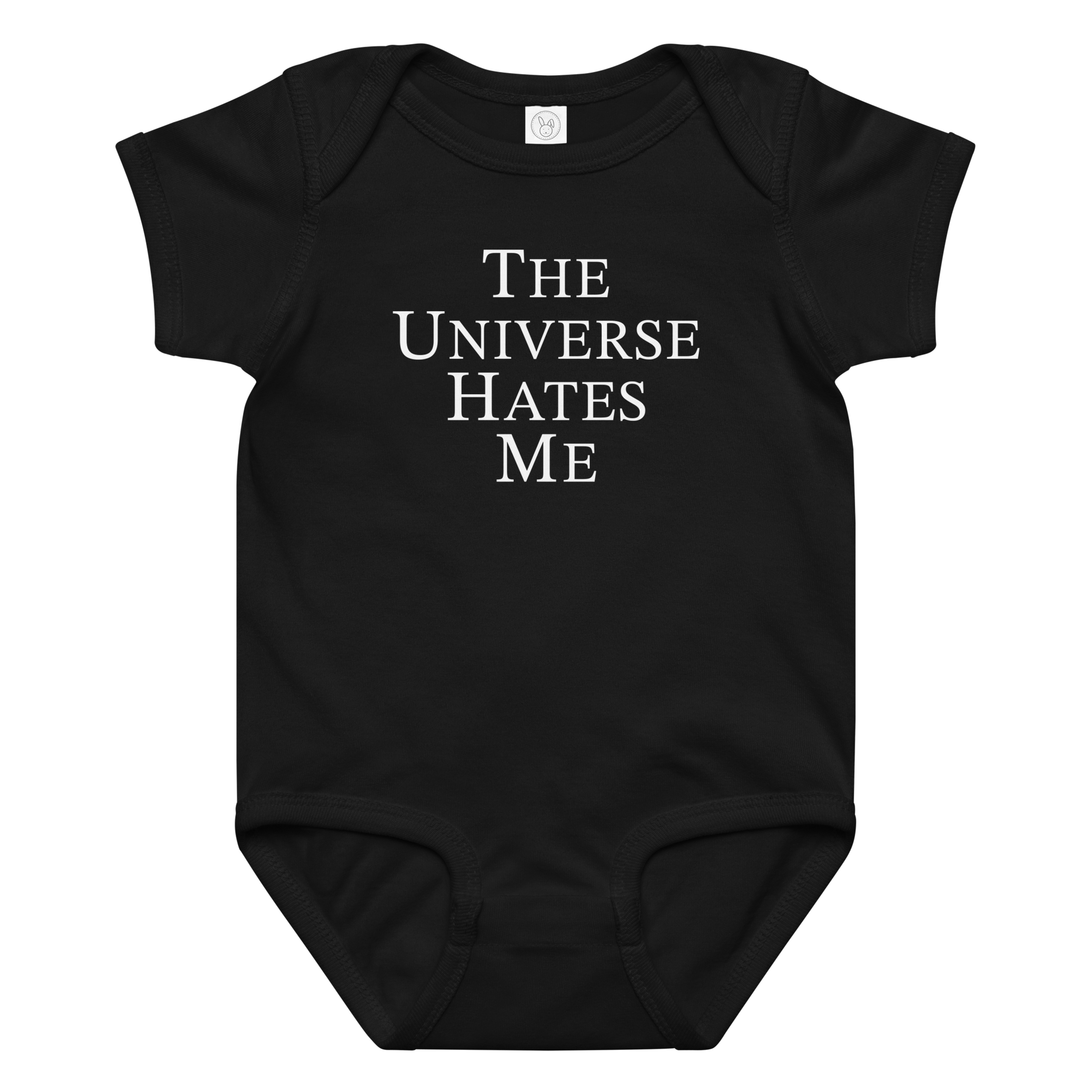 "The Universe Hates Me" printed on a black baby jersey bodysuit laying on a flat surface amongst other clothes