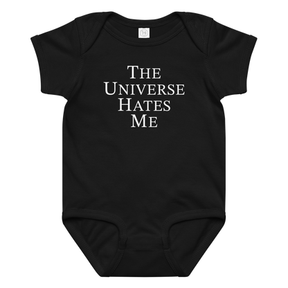 "The Universe Hates Me" printed on a black baby jersey bodysuit laying on a flat surface amongst other clothes